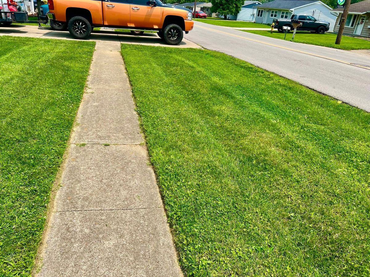A sidewalk with a clean cut edge of grass on both sides, the orange service truck parked at the top of the drive.