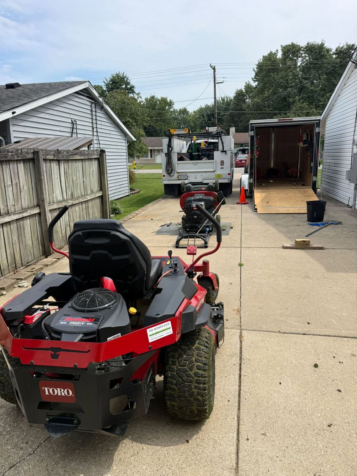 The red Toro zero-turn on a driveway with the walk-behind mower and the service truck behind it.